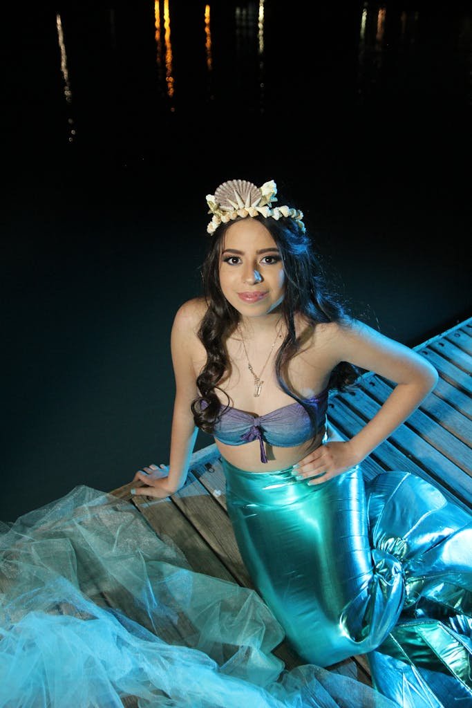 A young woman poses gracefully on a dock, dressed in a vibrant mermaid costume.