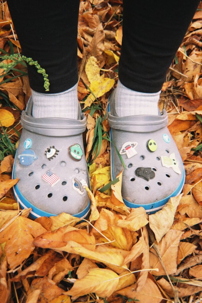 Someone wearing crocs and standing in fall leaves. There are Halloween pins in the crocs to show off your personality while you complete your Halloween bucket list.